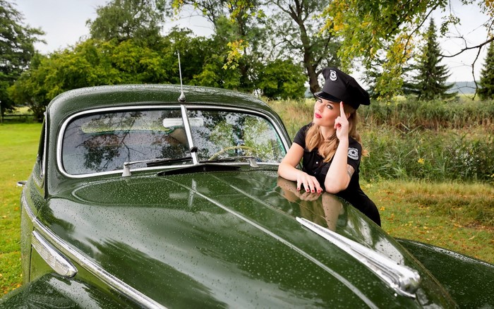 Woman in police uniform leaning on a vintage green Buick