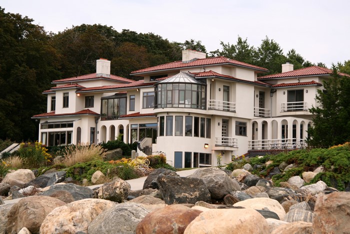 Large white mansion with red tile roof on rocky shore