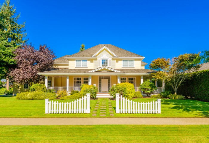 Yellow two-story house with white picket fence and lawn