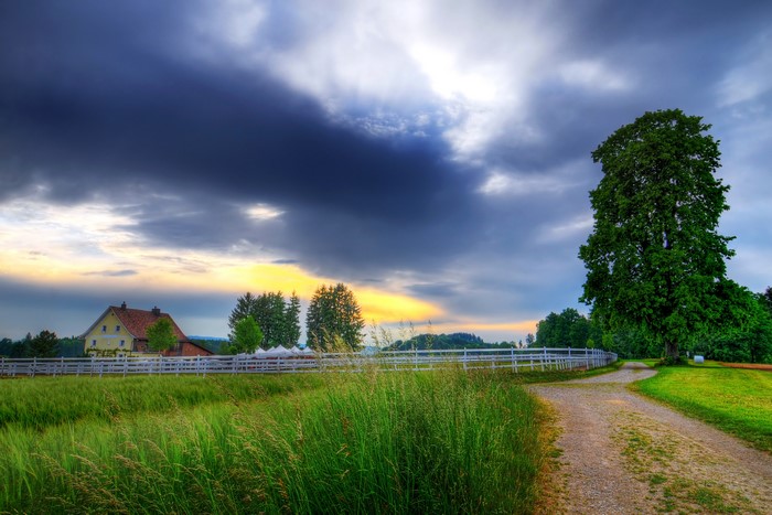 Farmhouse with a dirt road and dramatic clouds