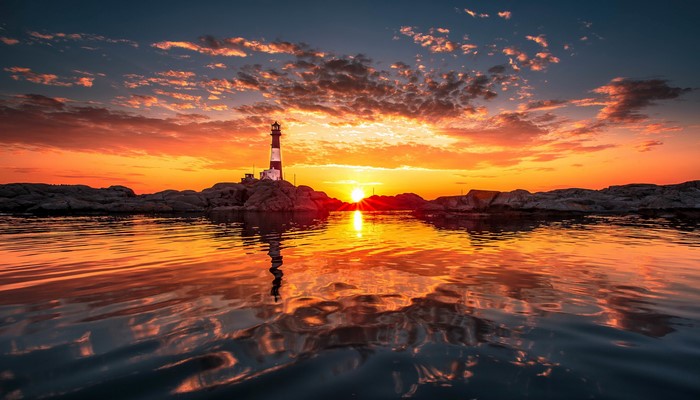 Lighthouse on rocky shore during sunset with reflection