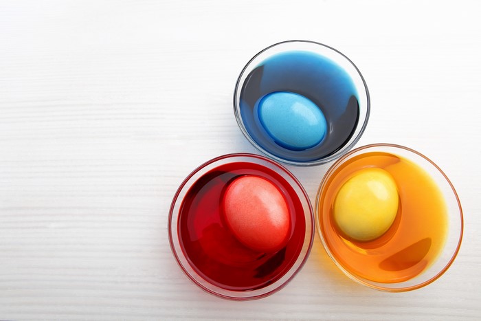 Easter eggs being dyed in red, yellow, and blue bowls