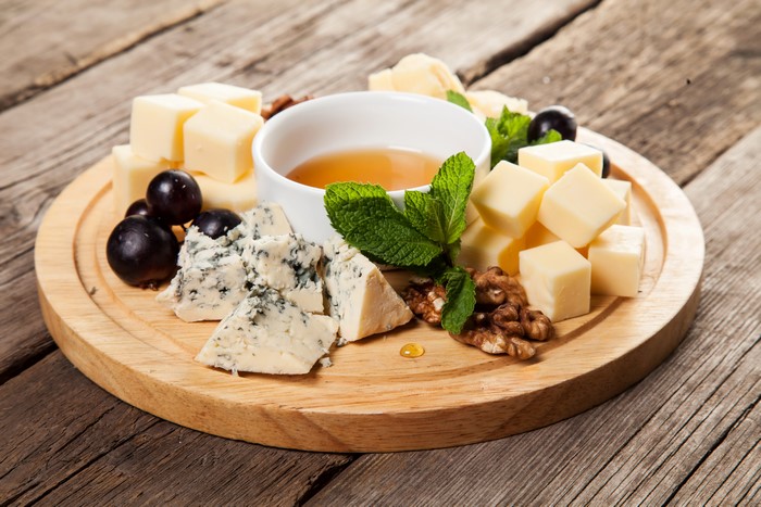 Cheese board with honey, grapes, nuts, and mint