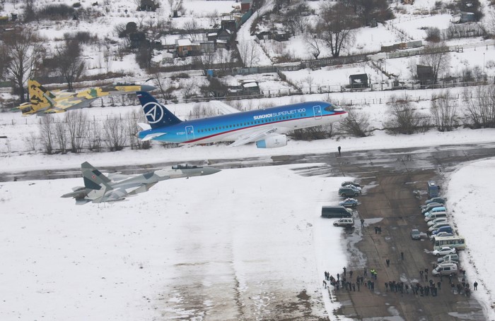 Sukhoi Superjet 100 and fighter jets on snowy airfield