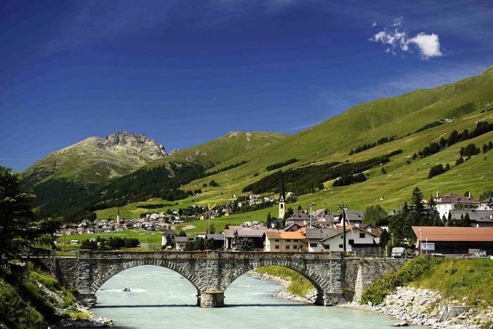 Stone bridge over a river in a Swiss village with mountains