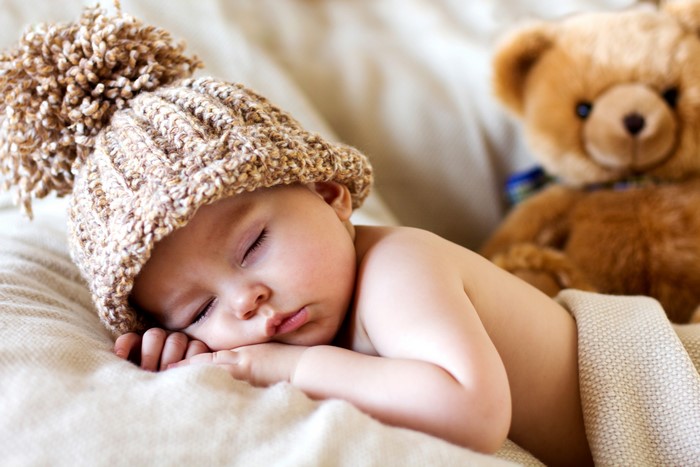 Baby sleeping with teddy bear wearing winter hat