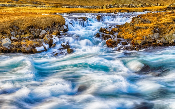 Fast flowing river with rocky banks and golden grass