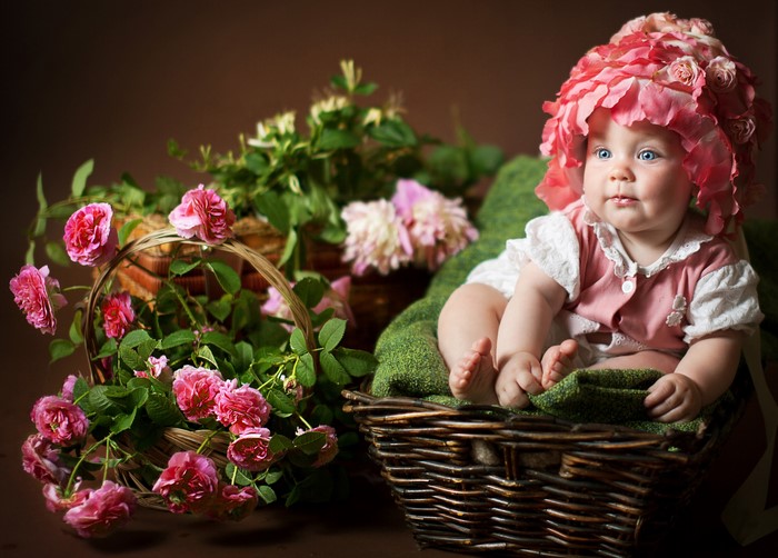 Baby in a flower hat sitting in a wicker basket with roses