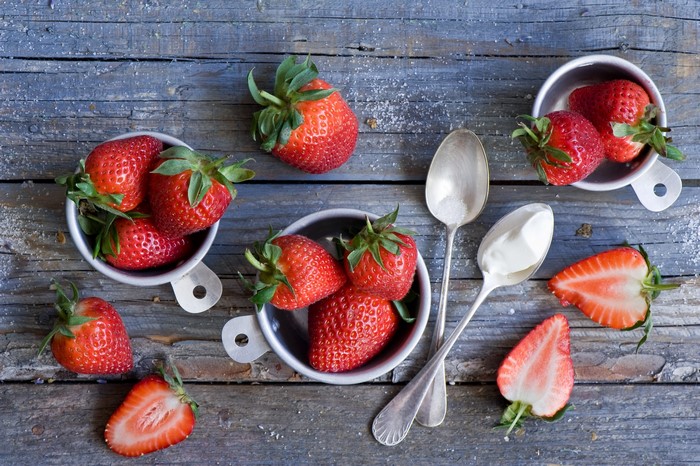 Strawberries in metal cups with spoons and cream