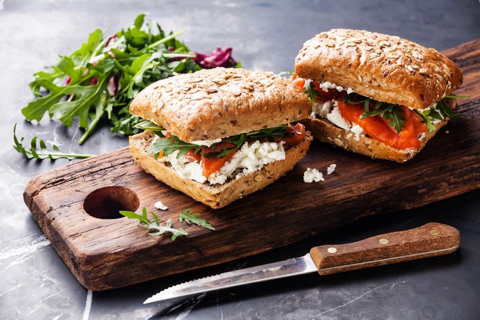 Two salmon sandwiches with feta and arugula on a wooden board with a knife
