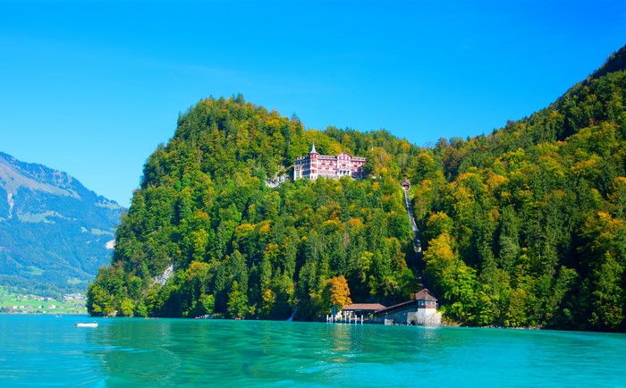 Hotel on a forested hill overlooking a turquoise lake in Switzerland