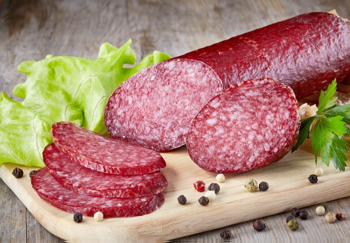 Sausage slices with lettuce and peppercorns on a cutting board
