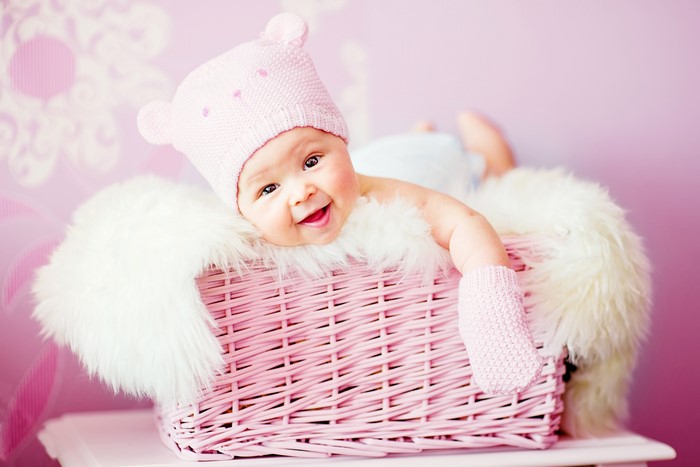 Baby in a pink hat and mittens in a wicker basket