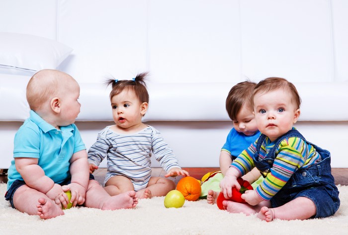 Four babies playing with fruit on a rug