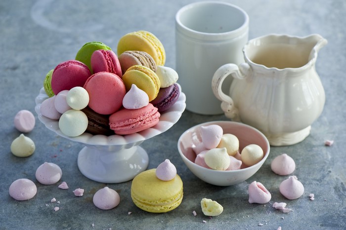 Colorful macarons and meringues on a cake stand with a jug