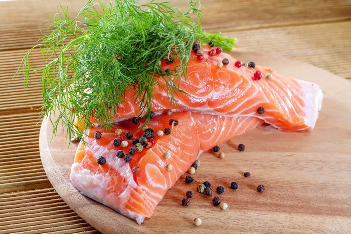 Salmon fillets with dill and peppercorns on a wooden board