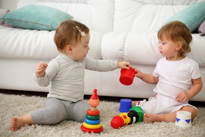Two Infants Playing with Toys on a Sofa