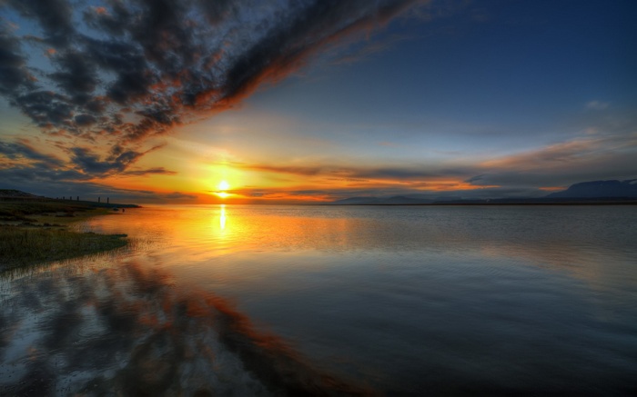 Sunset over a calm body of water with dramatic clouds