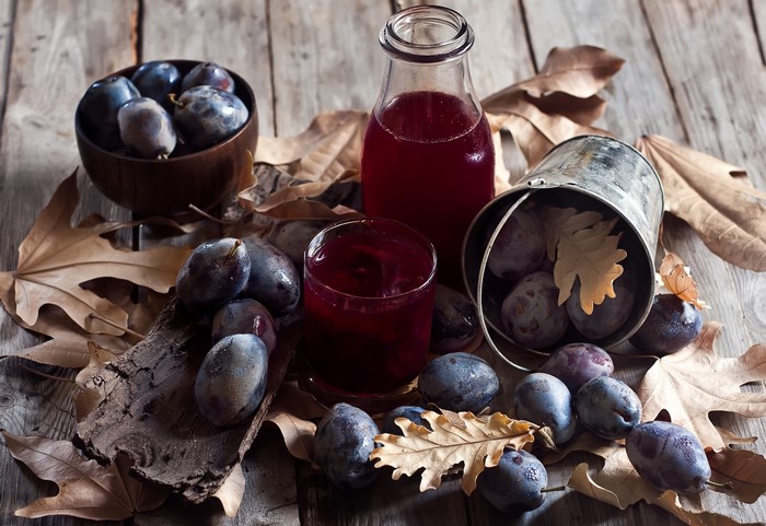 Plum juice and plums on a wooden table with autumn leaves