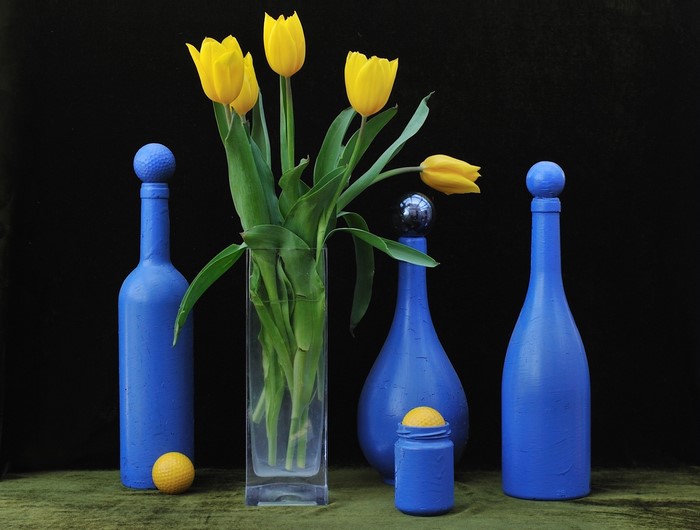 Yellow tulips in a vase with blue bottles and golf balls
