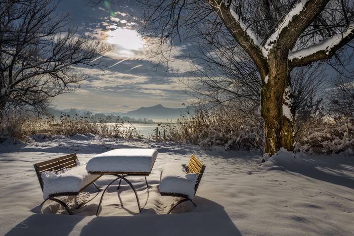 Winter scene with snow-covered table and benches by a lake
