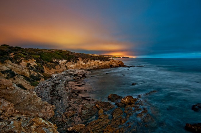 Rocky Coastline at Dusk with City Lights