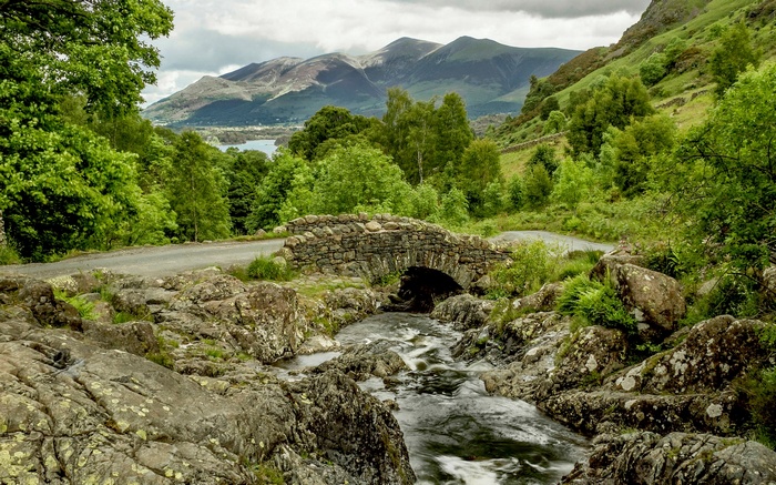 Stone bridge over a stream with mountains in the background