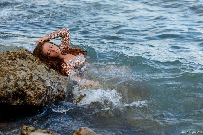 Woman in sequined dress lying on rocks in the sea