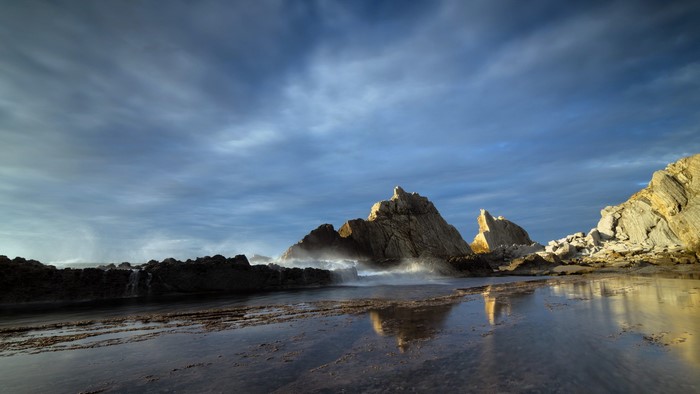 Waves crashing on rocky shore under cloudy sky