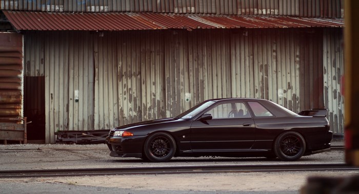 Black Nissan Skyline GT-R R32 parked near industrial building