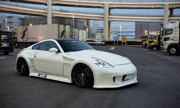 White Nissan 370Z parked in a lot with trucks