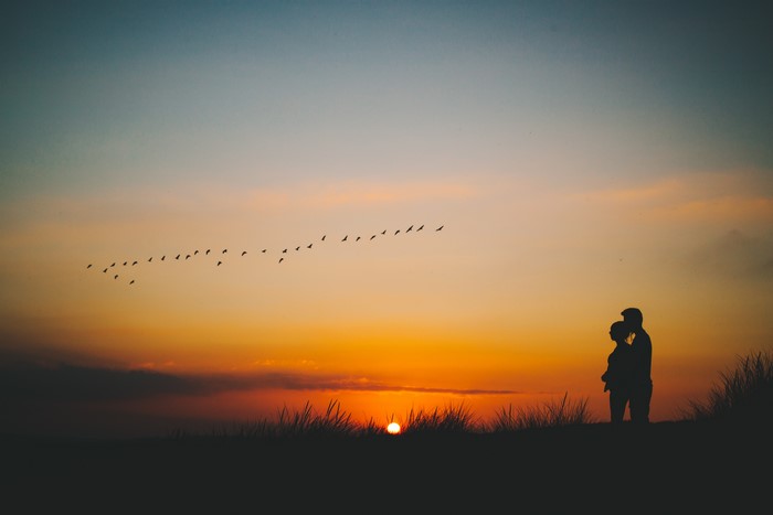Couple silhouetted against sunset with birds flying