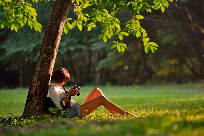 Woman with camera sitting under a tree in a park