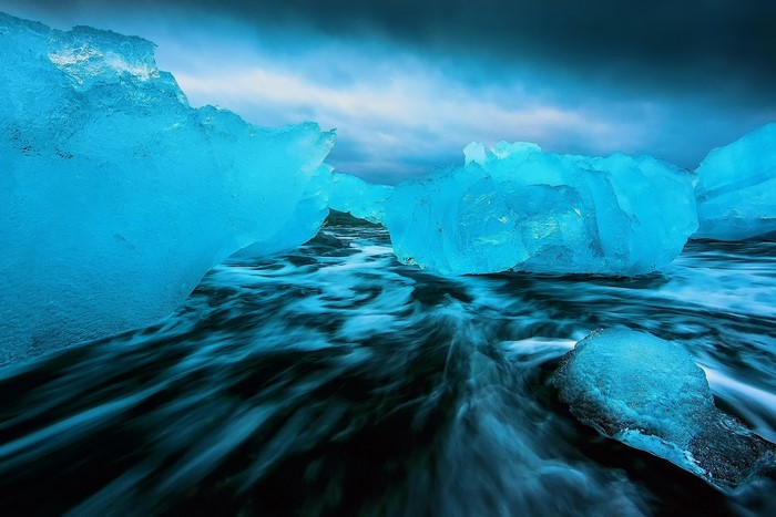 Blue icebergs on a black sand beach with ocean waves