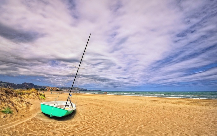 Sailboat on a sandy beach with cloudy sky
