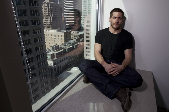 Jake Gyllenhaal sitting by a window overlooking skyscrapers