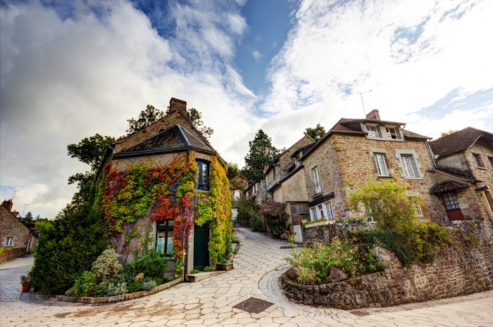 Stone houses covered in ivy on a cobblestone street in Saint Ceneri le Gerei, France