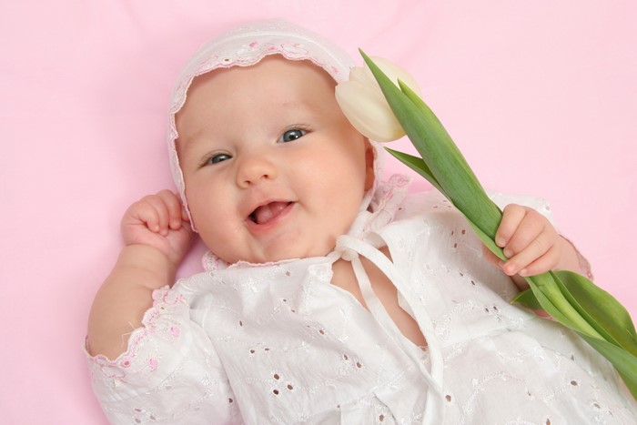 Baby in bonnet holding a white tulip