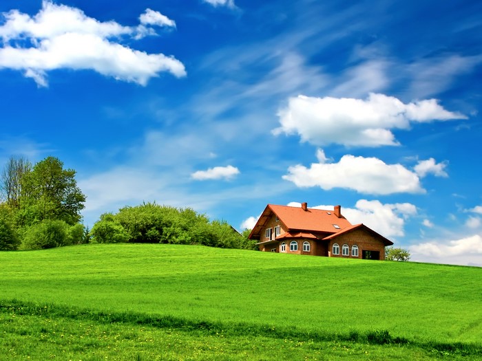 House on a green hill under a blue sky with clouds