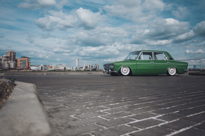 Green VAZ 2103 Lada parked on brick pavement with city skyline