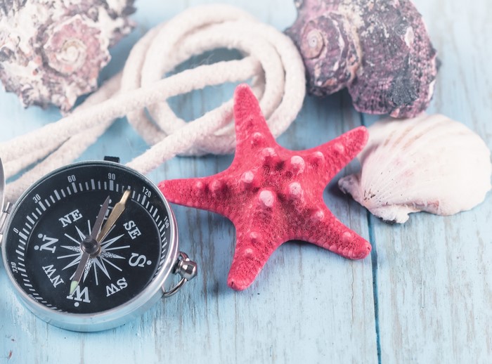 Compass, starfish, rope, and seashells on a wooden surface