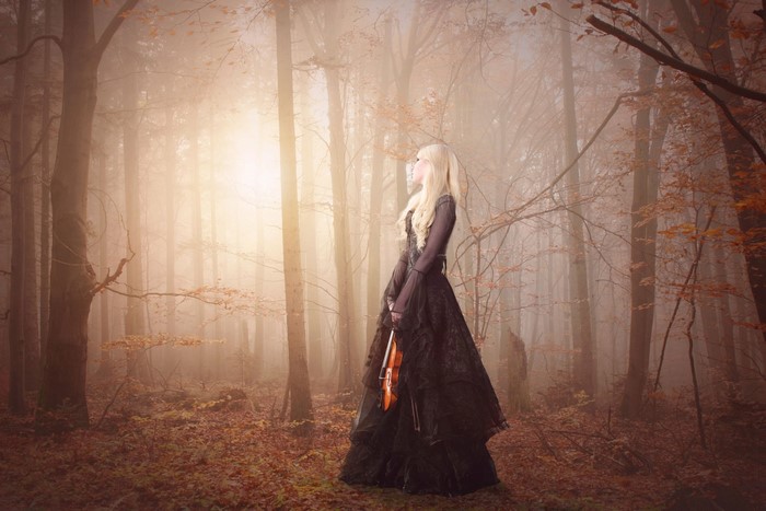 Woman in black dress holding a violin in a foggy forest