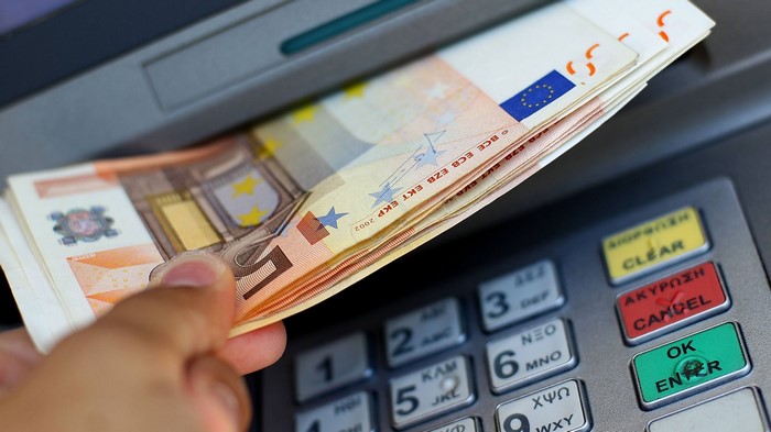 Hand holding Euro banknotes at ATM keypad