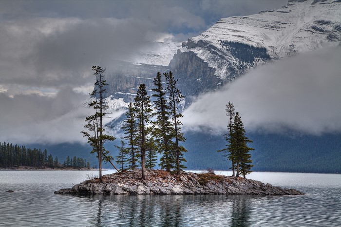 Island with trees in a lake with snowy mountains and clouds