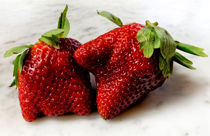 Two oddly shaped strawberries on a marble surface