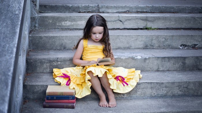 Young girl in yellow dress reading on stairs with books