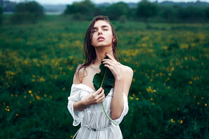 Woman in white dress holding a leaf in the rain