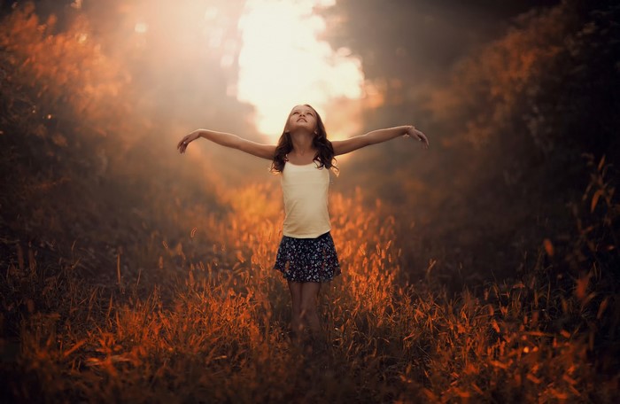 Girl Standing in Sunlit Grass with Arms Outstretched