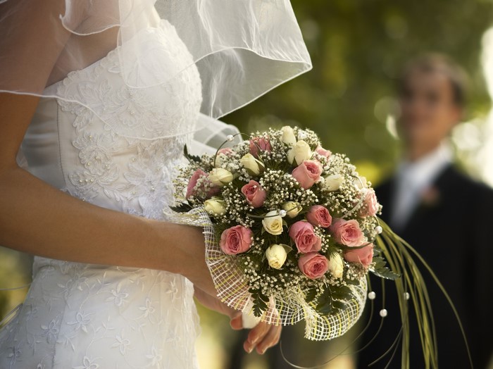 Bride holding a bouquet with groom in background