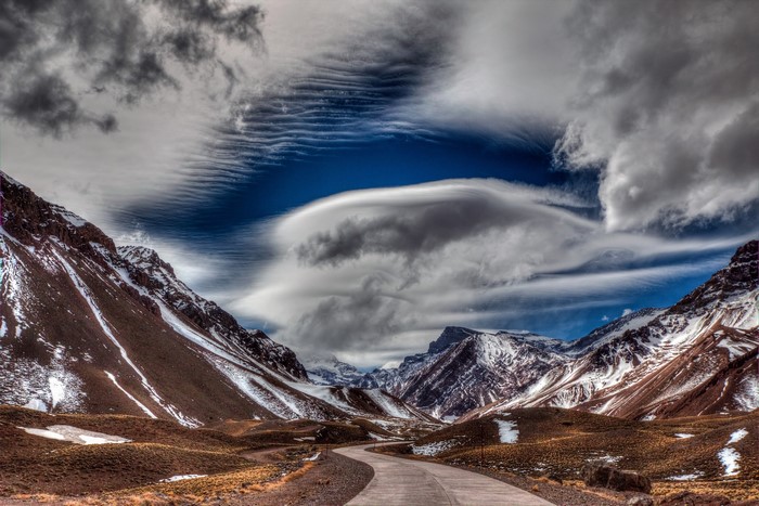 Winding road through snow-capped mountains under dramatic clouds